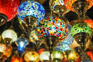 A collection of colorful mosaic lanterns hanging from the ceiling. The lanterns feature vibrant stained glass patterns in red, blue, green, and yellow, each with intricate detailing and brass fixtures, creating a warm, inviting atmosphere.